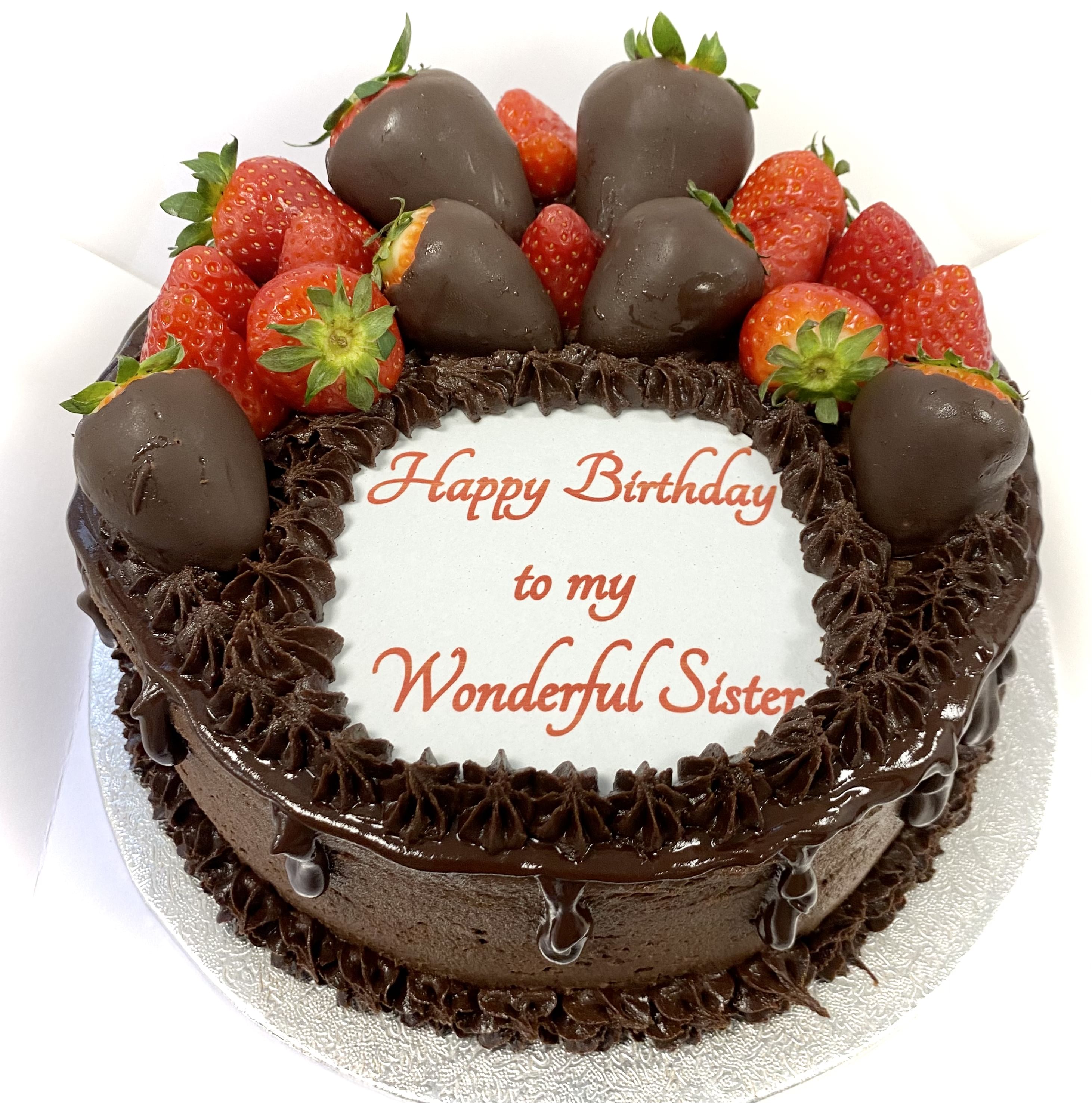 A decadent chocolate cake topped with chocolate-covered strawberries and fresh strawberries arranged around the edges. This irresistible dessert boasts a white icing plaque in the center with the message 'Happy Birthday to my Wonderful Sister' written in red.